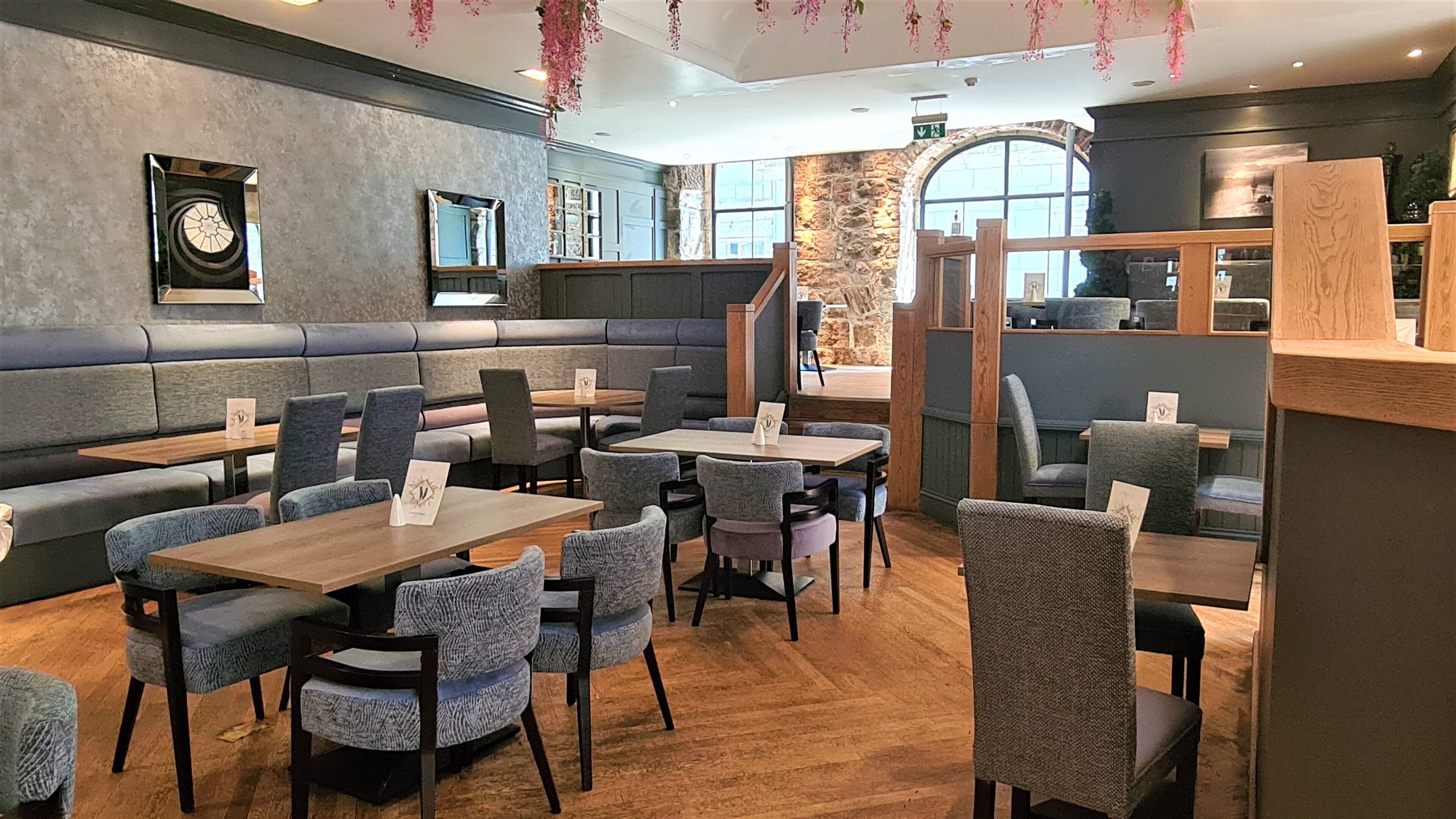 Un restaurante con cabinas y mesas, paredes de piedra y plantas colgantes.