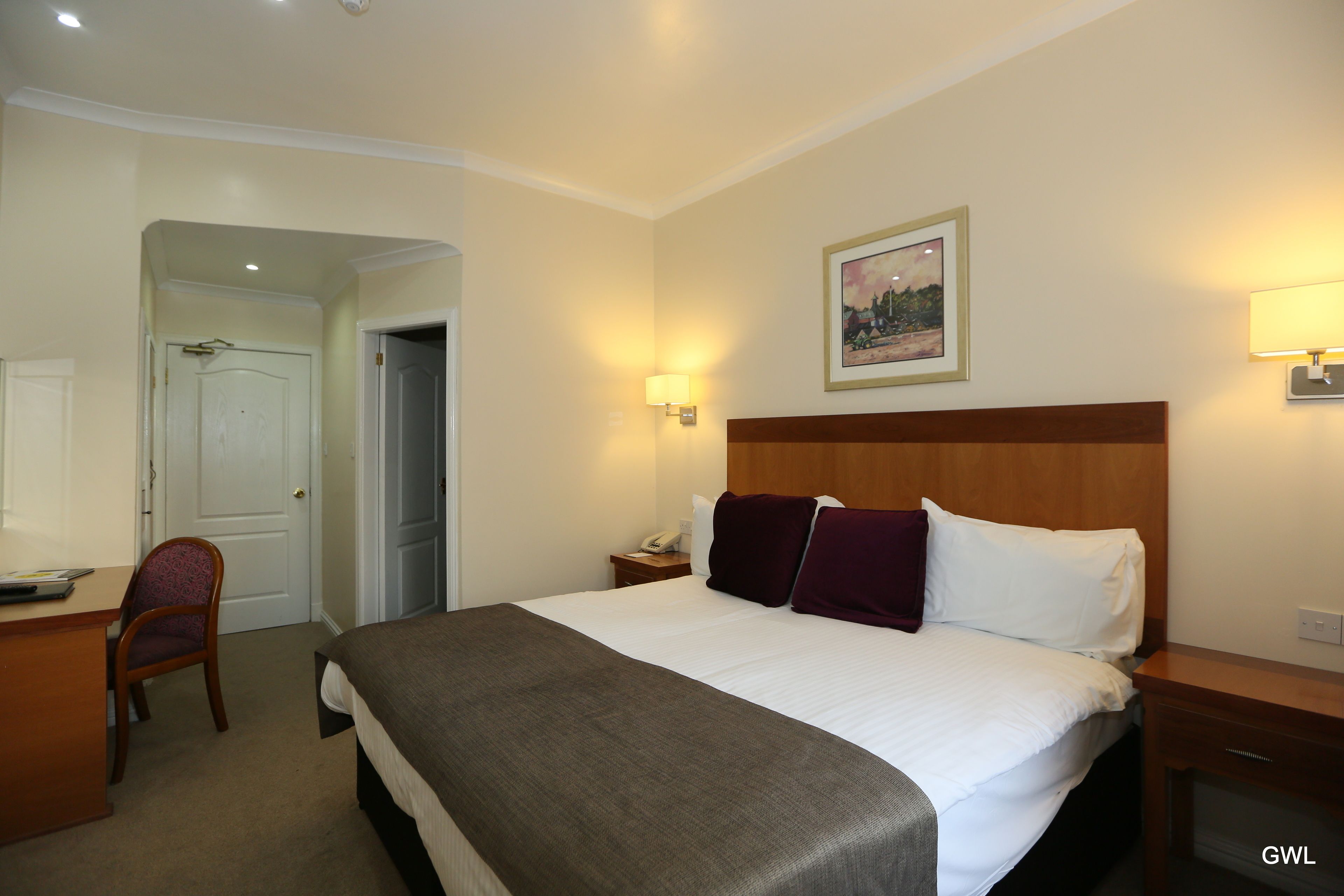 A hotel room with a bed, a desk, a chair, and a nightstand.