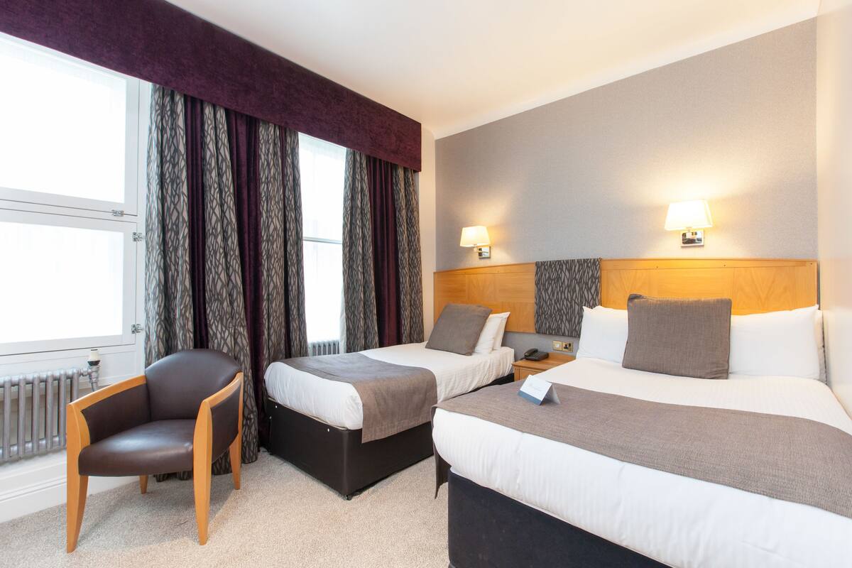 A hotel room with two beds, a chair, a bedside table, and a lamp.