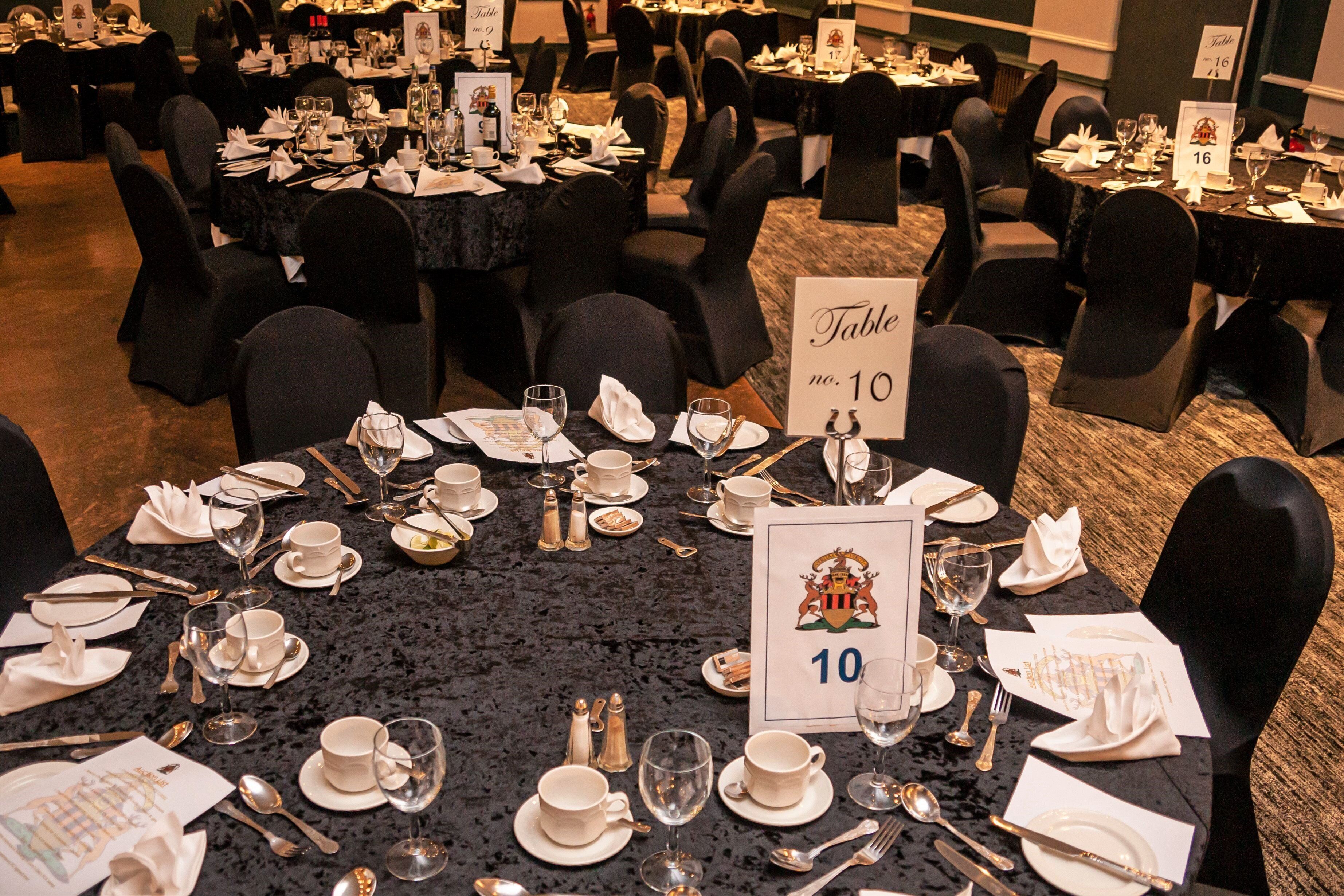 A banquet hall with round tables, each set with white tableware and numbered place cards.