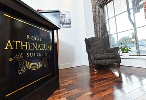 Un pianoforte nero con scritte dorate e una poltrona con motivo decorativo in una stanza con pavimento in legno e una finestra con persiane.