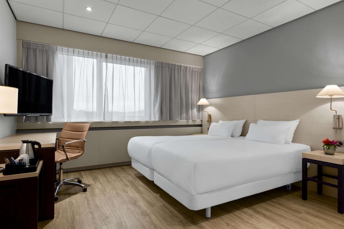 A hotel room with a bed, desk, chair, TV, and lamps.