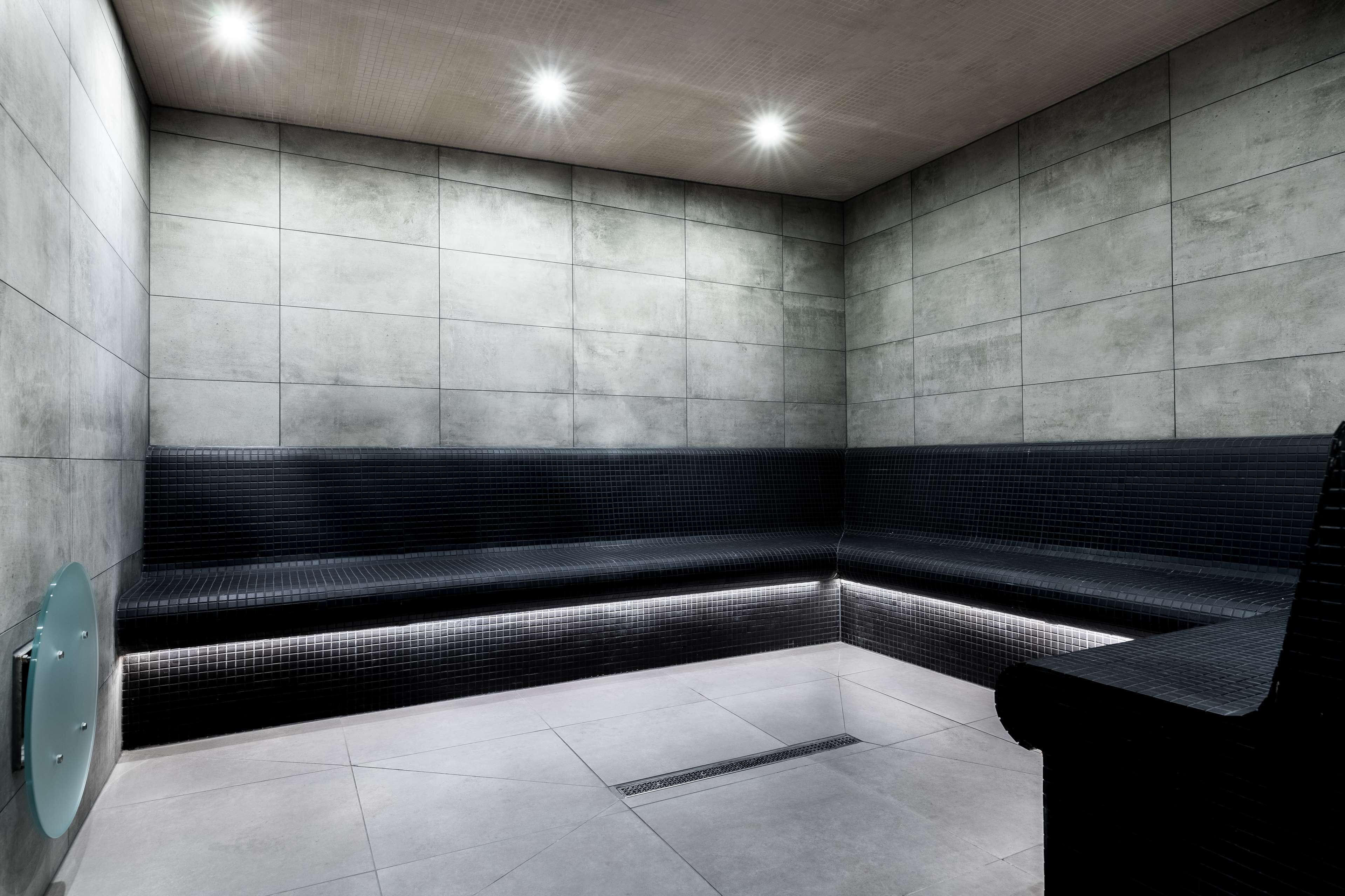 A modern, minimalist bathroom with a black tiled bench and a glass door.