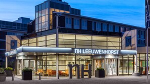 Een modern gebouw met een glazen gevel en een bordje met de tekst 'NH Leeuwenhorst'.