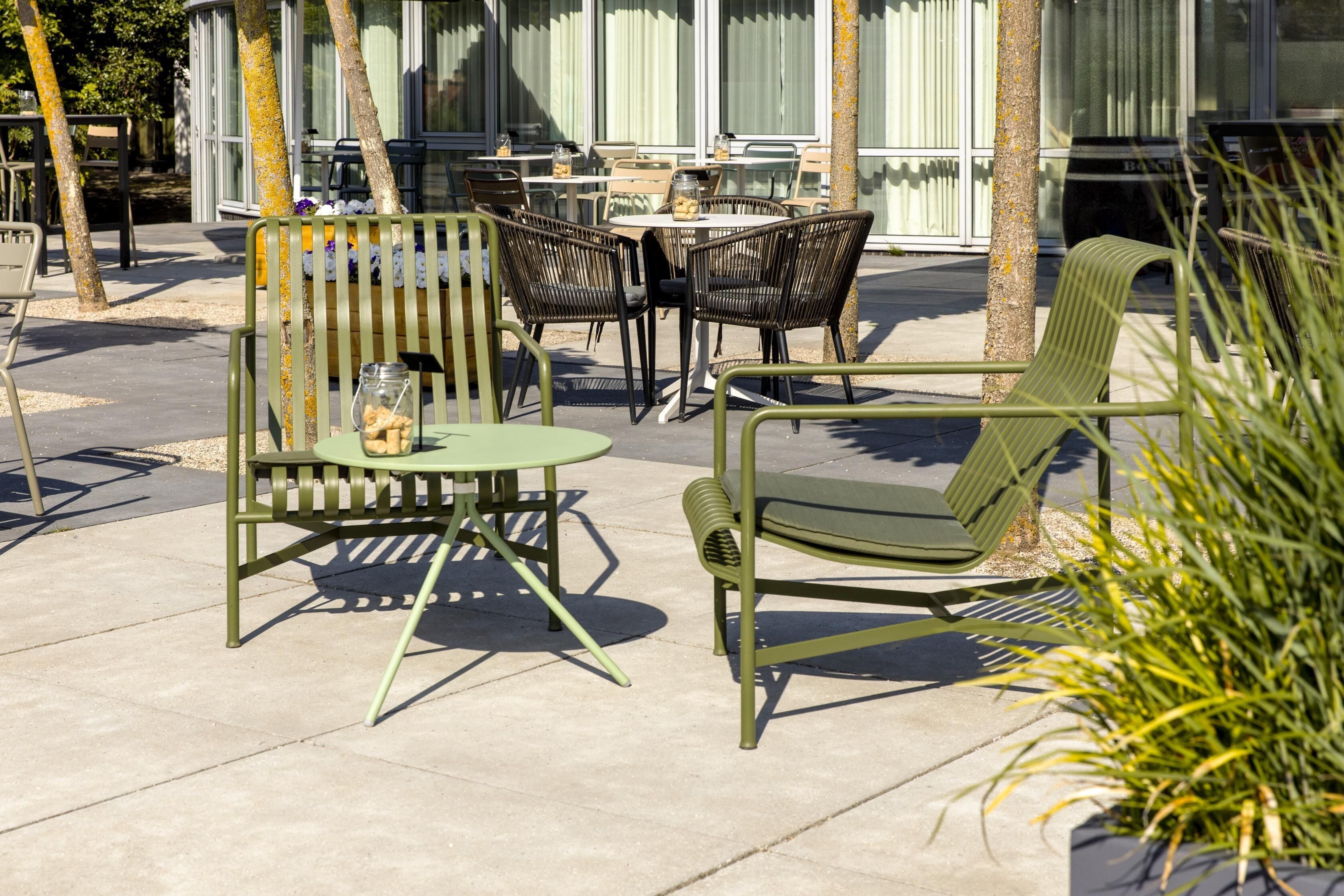 An outdoor seating area with metal chairs and tables, a small round table with a glass jar, and a potted plant.