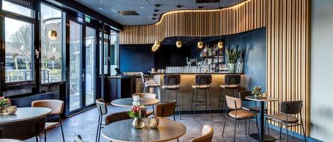 A modern restaurant interior with round tables, bar stools, and a counter with a wooden panel design.