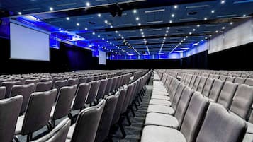 Ein großes Innenraum-Auditorium mit Reihen grauer Stühle und einer großen Leinwand im vorderen Bereich.