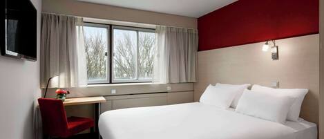 Une chambre d’hôtel avec un lit, un bureau, une chaise, une télévision et une fenêtre avec des rideaux.