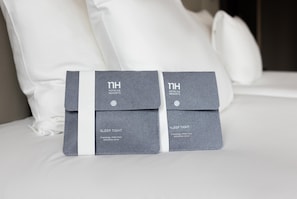 Two grey sleep tight packages on a bed with white pillows. - NH Amsterdam Caransa (Amsterdam)