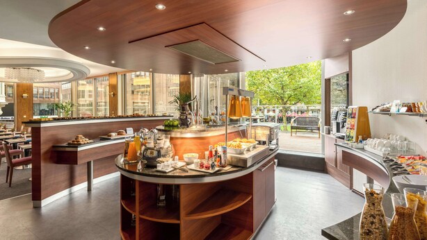 A modern breakfast area with a central island, seating, and a view of the outdoors. - NH Amsterdam Caransa (Amsterdam)