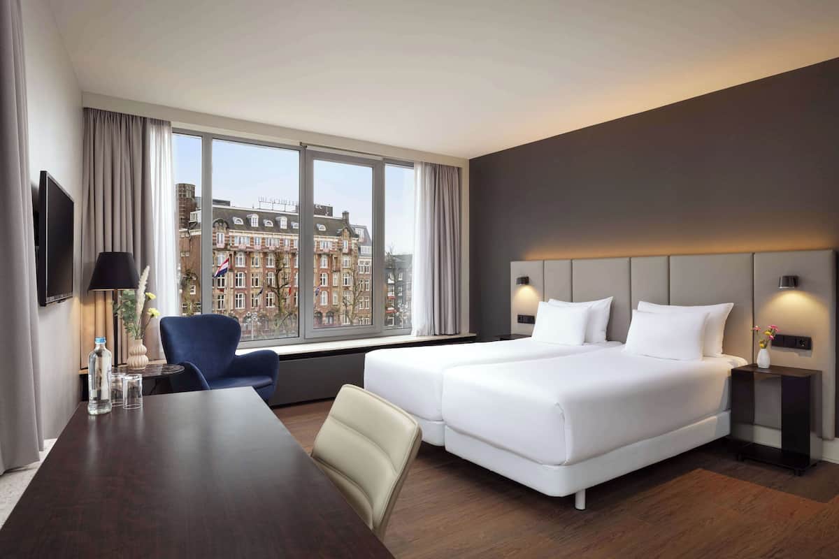 A hotel room with a large window, a bed, a desk, and a chair.
