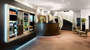 A modern hotel lobby with a reception desk, a staircase, and a seating area. - NH Amsterdam Caransa (Amsterdam)
