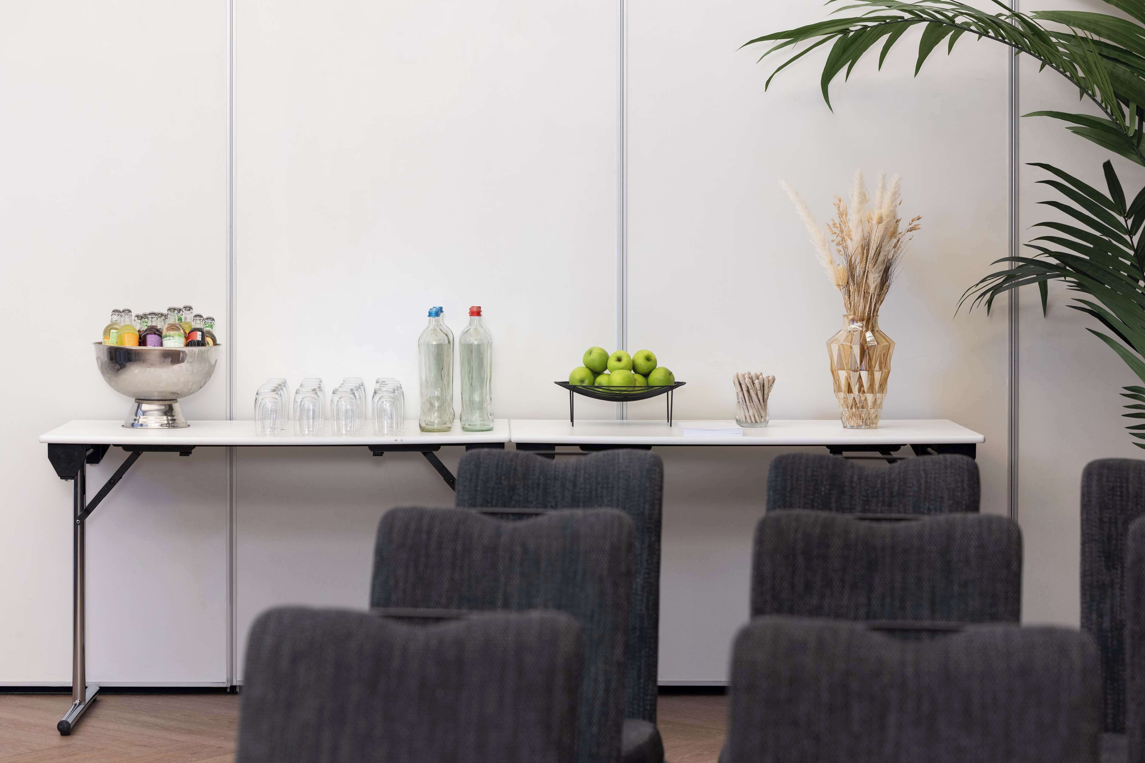 A conference room with a white table, grey chairs, a bowl of green apples, and a vase with dried plants.