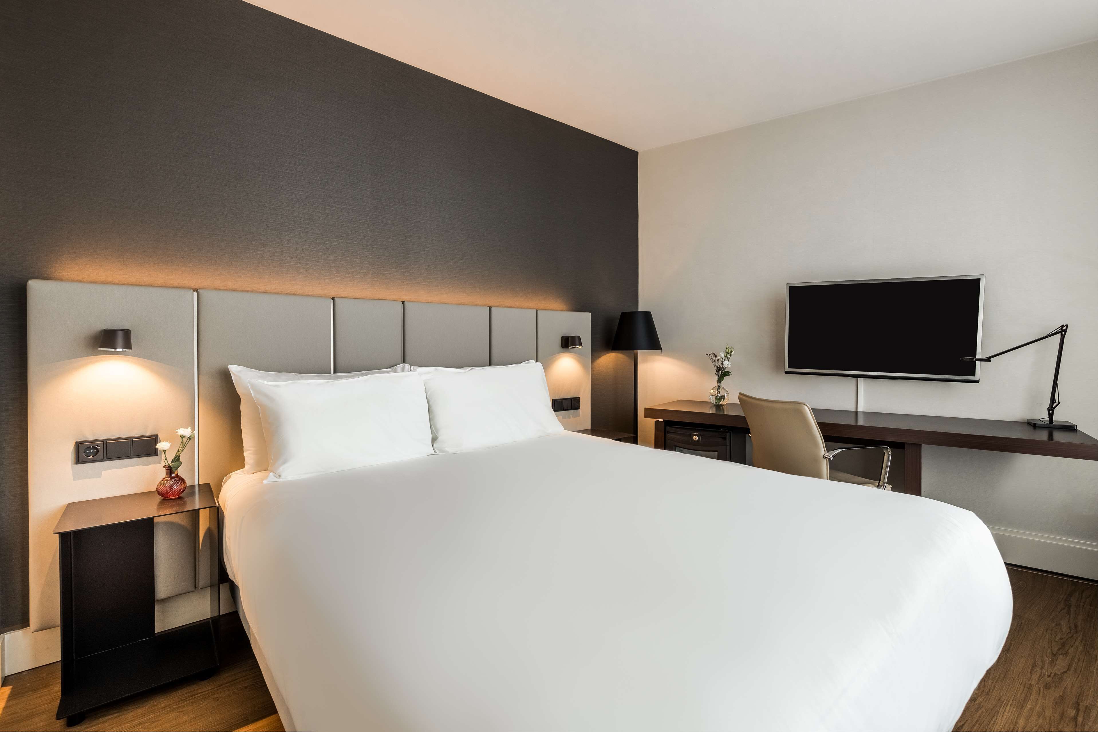 A modern hotel room with a large bed, bedside tables, a desk, and a flat-screen TV.
