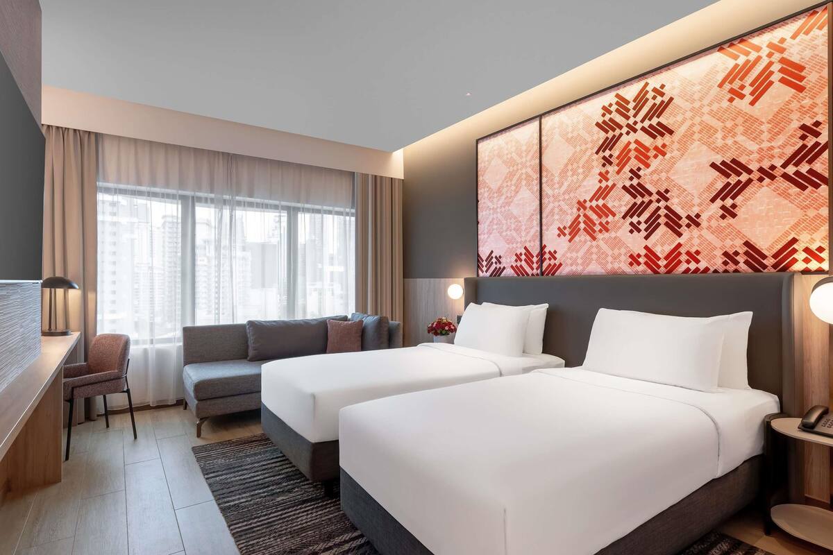 Ein Hotelzimmer mit zwei Betten, einem Schreibtisch, einem Sofa und einem großen Fenster mit Vorhängen.