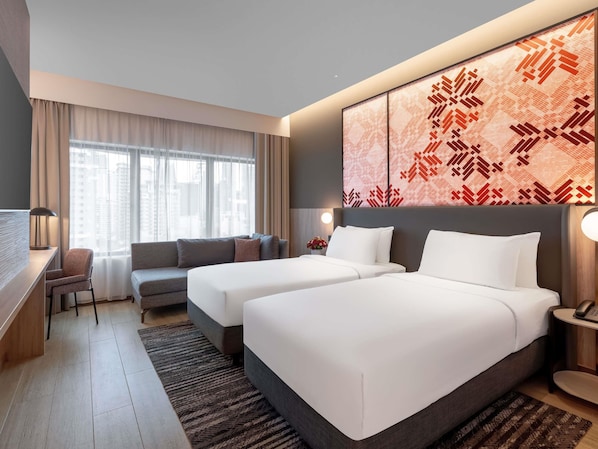 A hotel room with two beds, a desk, a sofa, and a large window with curtains.