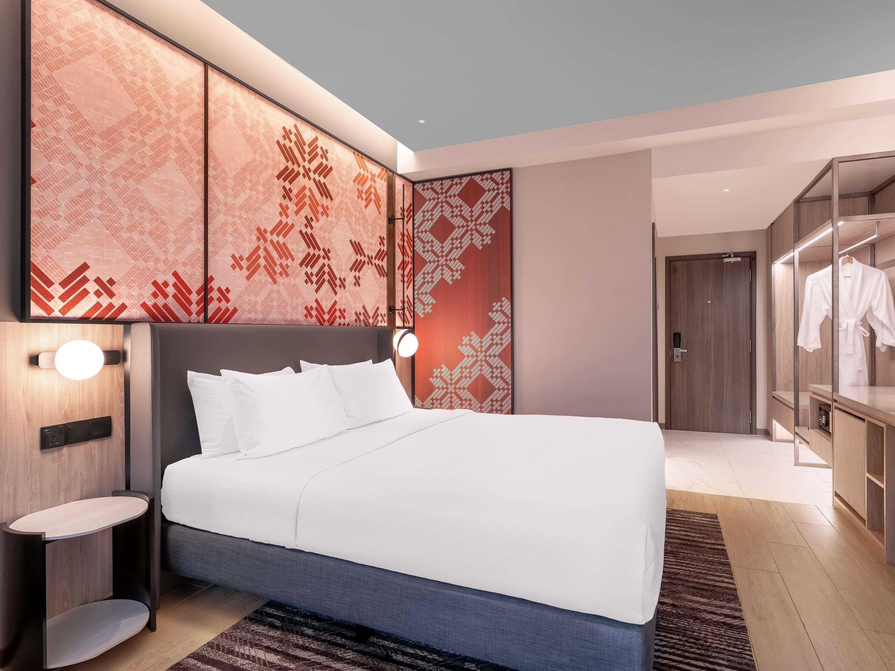 Een moderne hotelkamer met een groot bed, nachtkastjes, een kledingkast en een decoratieve wandbekleding.