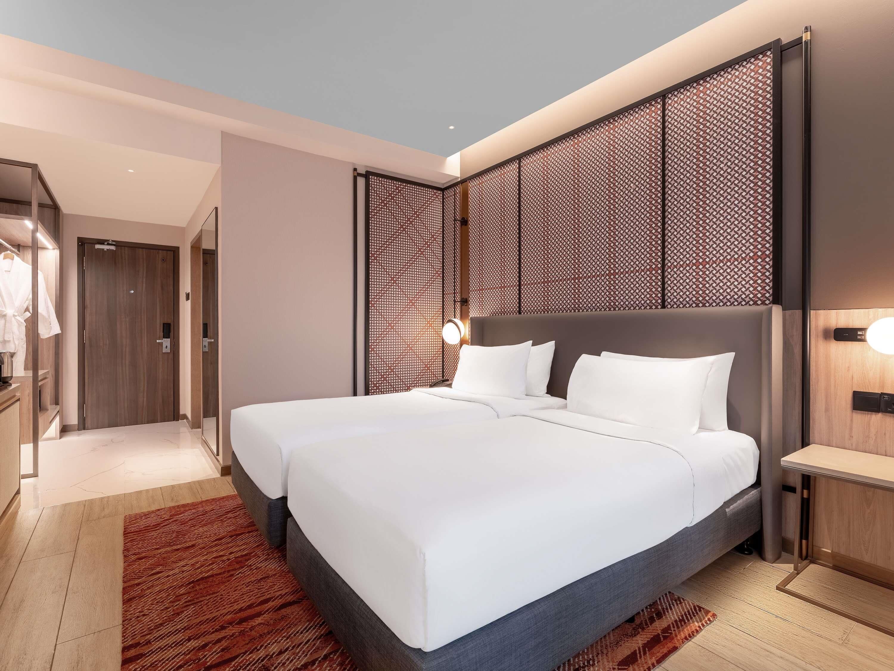 Ein modernes Hotelzimmer mit einem großen Bett, einem Nachttisch, einem Kleiderschrank und einer dekorativen Wandverkleidung.