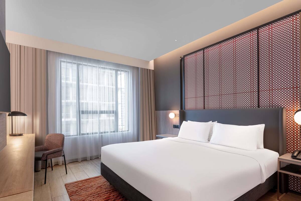 Ein modernes Hotelzimmer mit einem großen Bett, einem Schreibtisch, einem Stuhl und einer dekorativen Wandverkleidung.