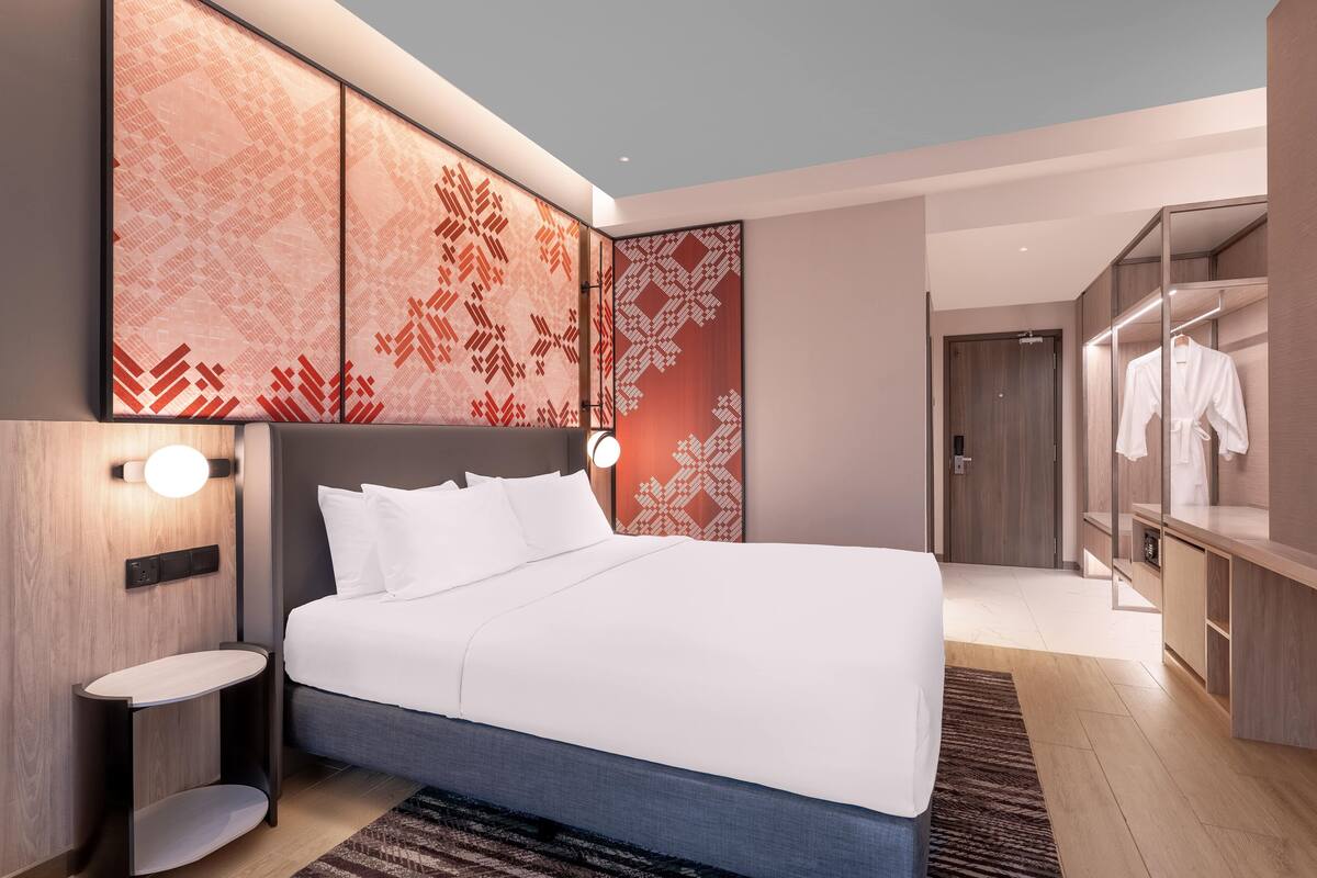 Ein modernes Hotelzimmer mit einem großen Bett, einem Nachttisch, einem Kleiderschrank und einer Wand mit geometrischem Muster.