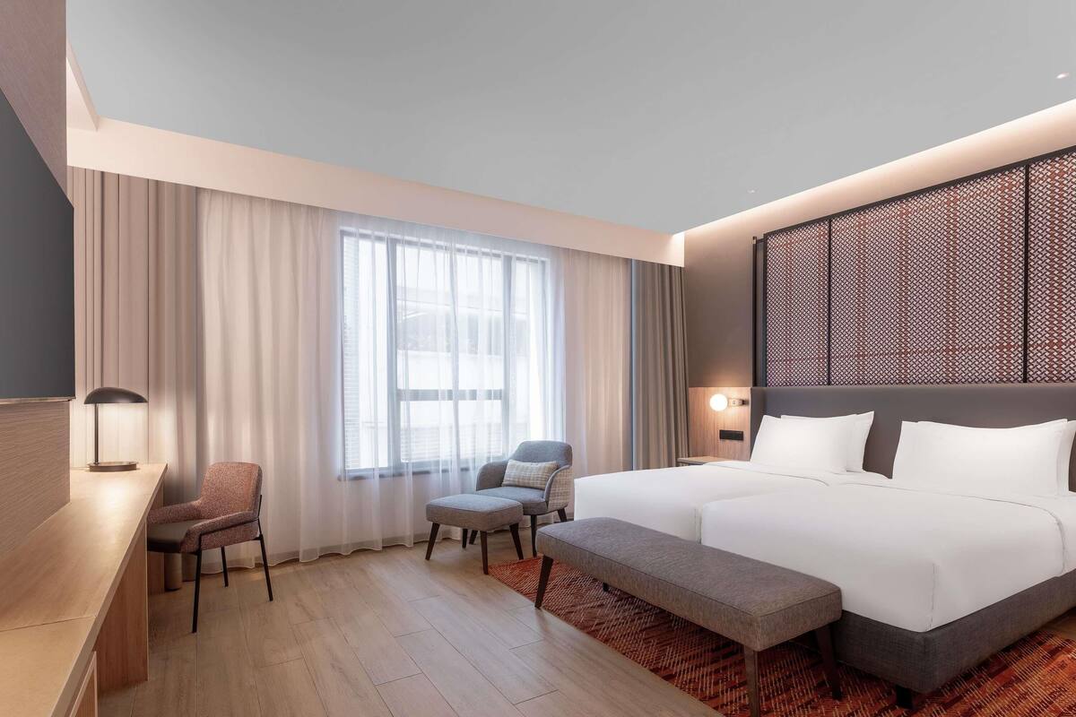 Ein Hotelzimmer mit einem großen Bett, einem Schreibtisch, einem Stuhl und einem fenster mit Vorhängen.