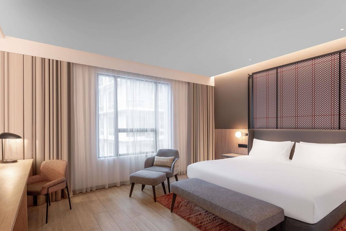 Ein modernes Hotelzimmer mit einem großen Bett, einem Schreibtisch, einem Sessel und einer Bank.