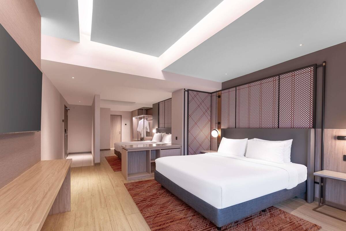 Ein modernes Hotelzimmer mit einem großen Bett, einem Schreibtisch, einem Spiegel und einem begehbaren Kleiderschrank.