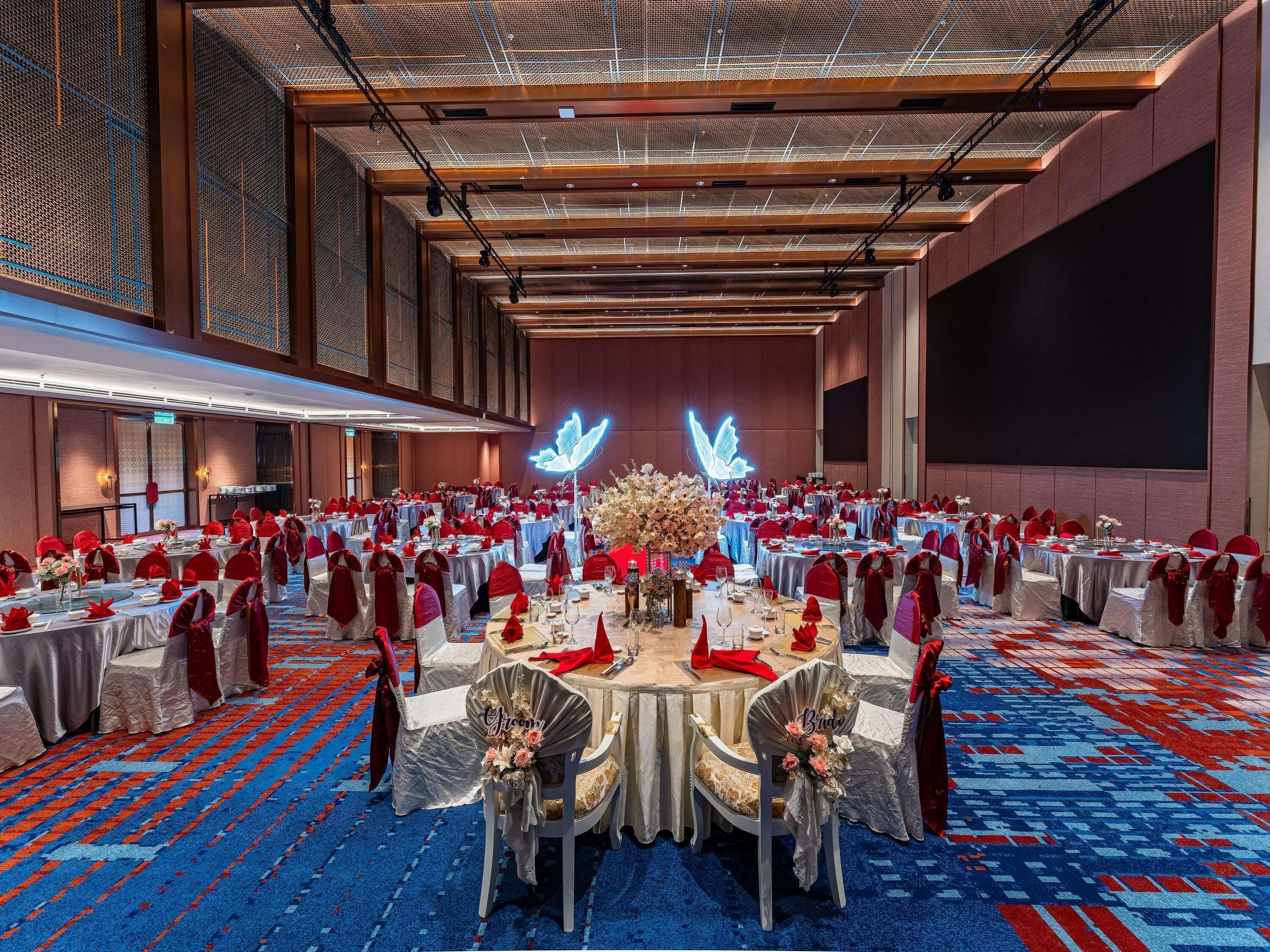 A banquet hall with round tables, red chairs, and a large floral centerpiece.