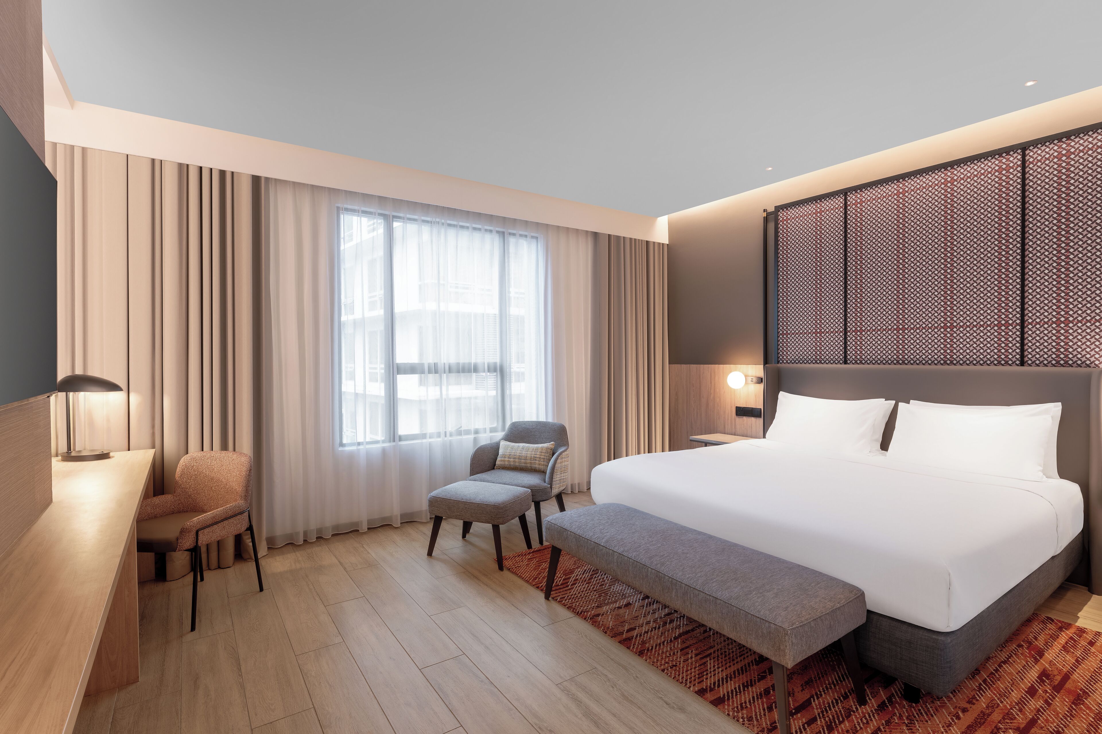 Een moderne hotelkamer met een groot bed, een bureau, twee stoelen en een groot raam met gordijnen.