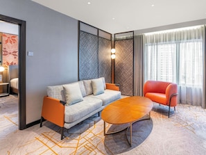 Moderni hotellihuone, jossa on sohva, punainen nojatuoli, puinen sohvapöytä ja kuviollinen matto.
