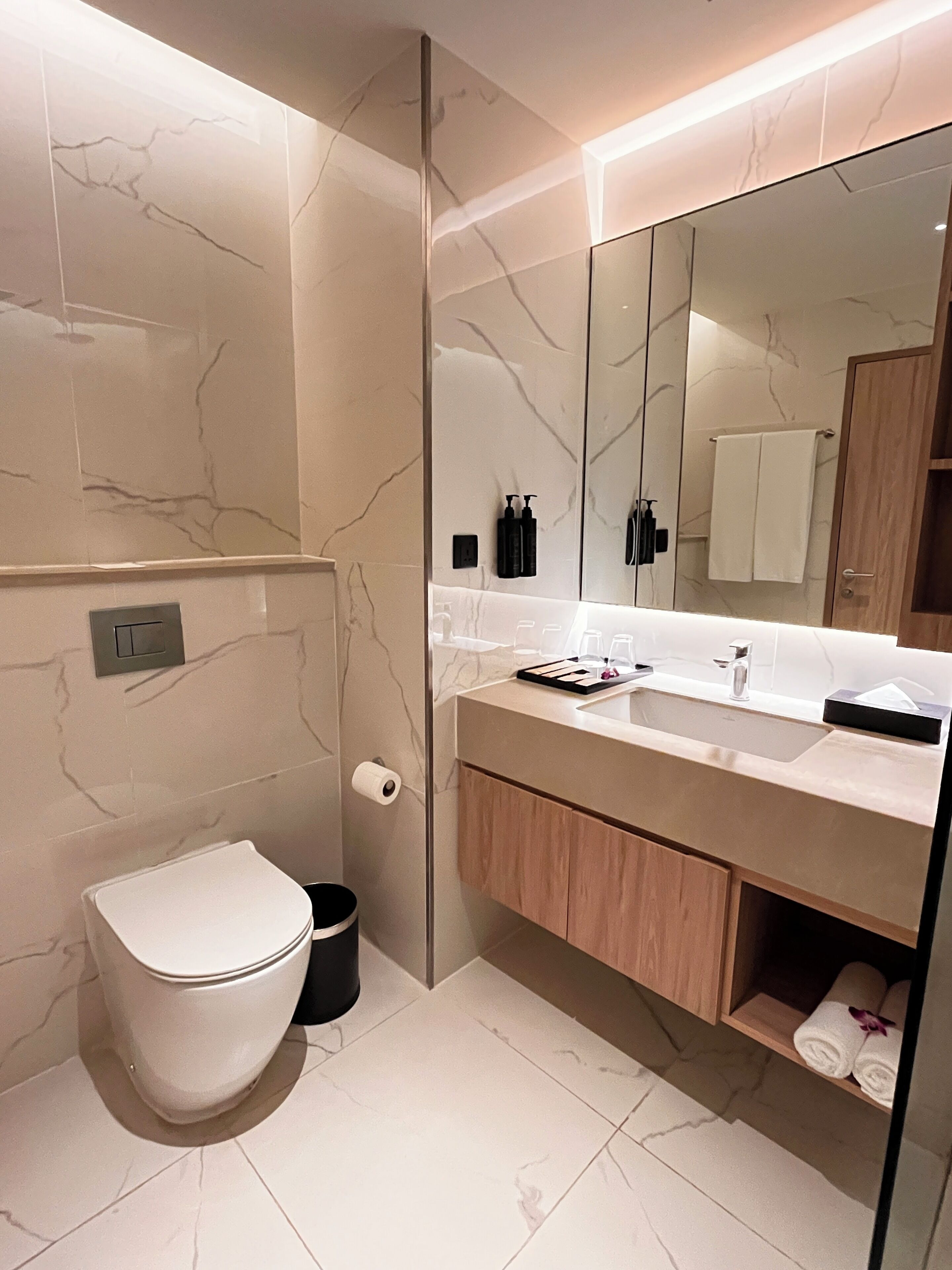A modern bathroom with a marble floor, a white toilet, a sink with a mirror, and wooden cabinets.