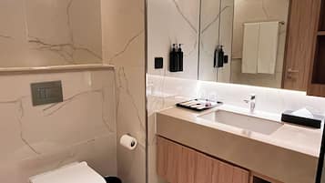 A modern bathroom with a marble floor, a white toilet, a sink with a mirror, and wooden cabinets.