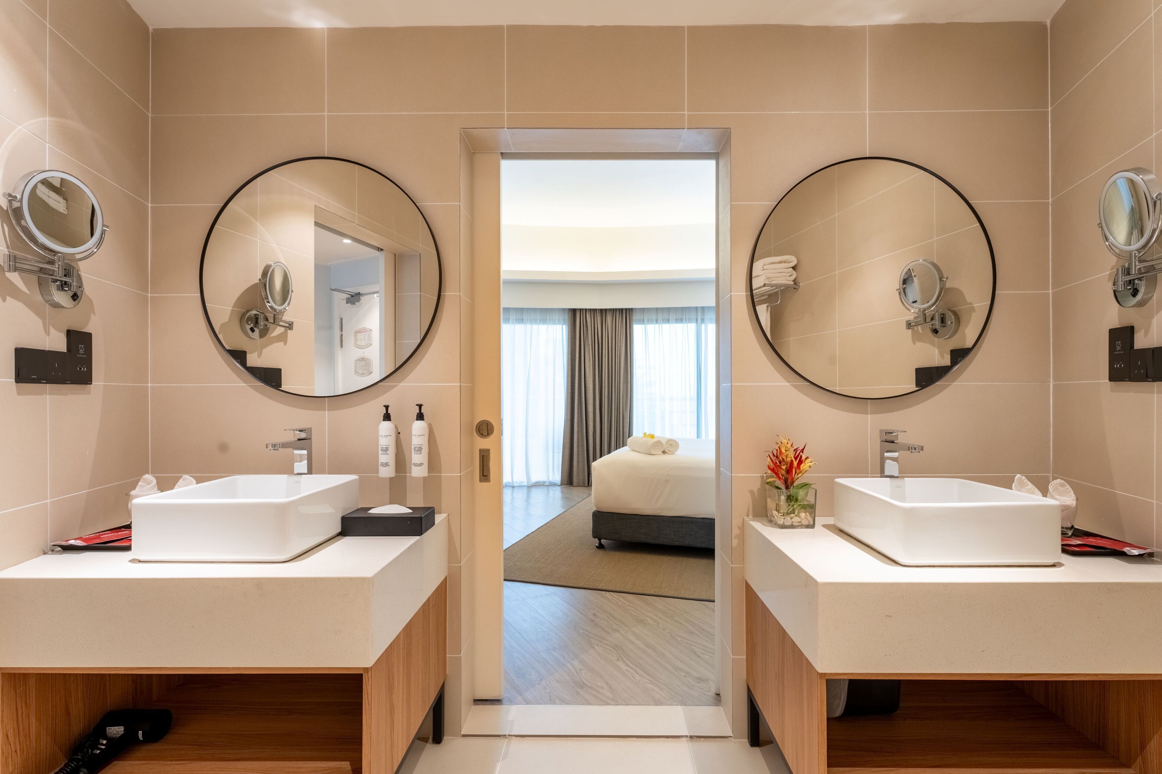 A modern bathroom with two sinks, mirrors, and a view into a bedroom.