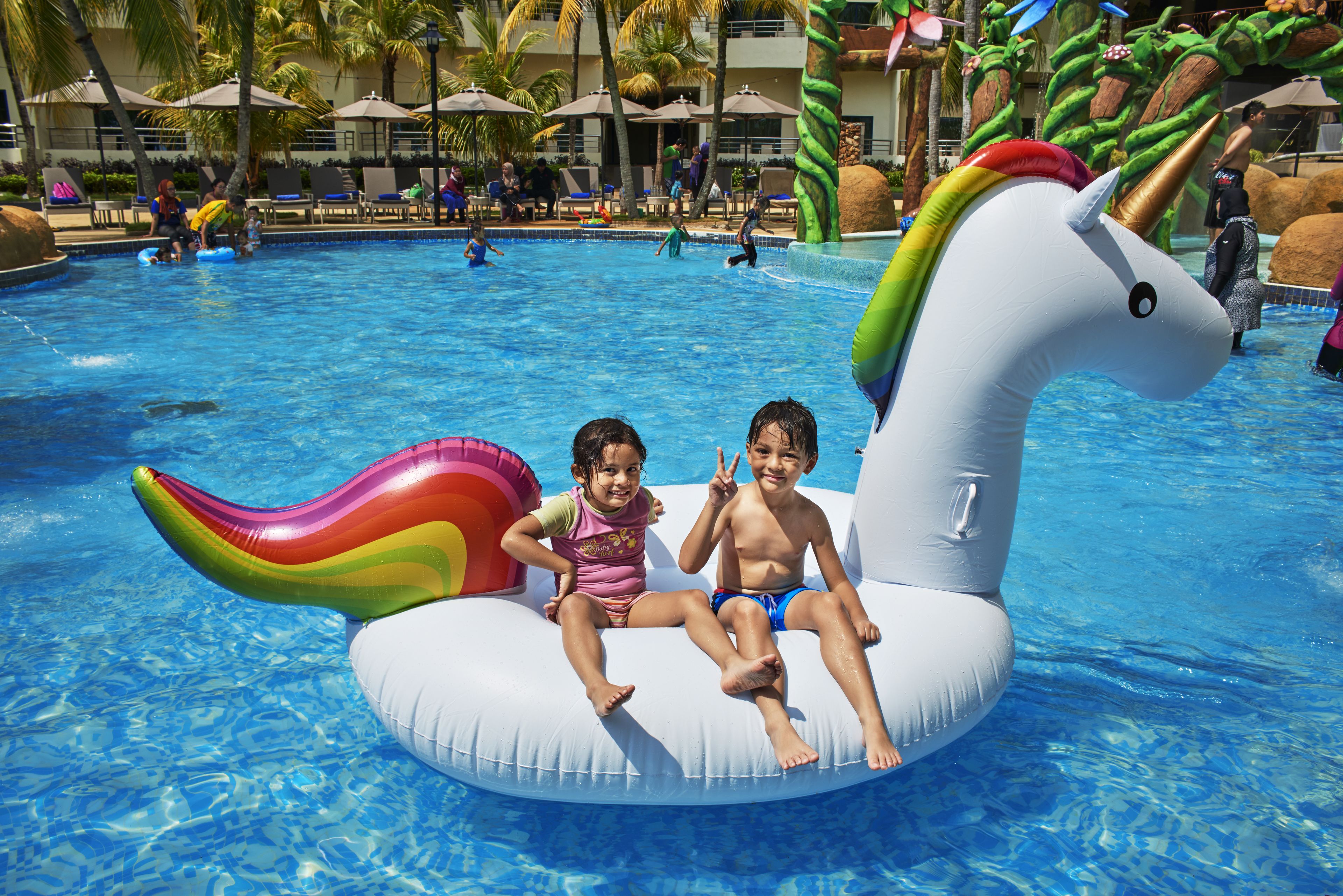 A pool with inflatable unicorn floats and palm trees in the background.
