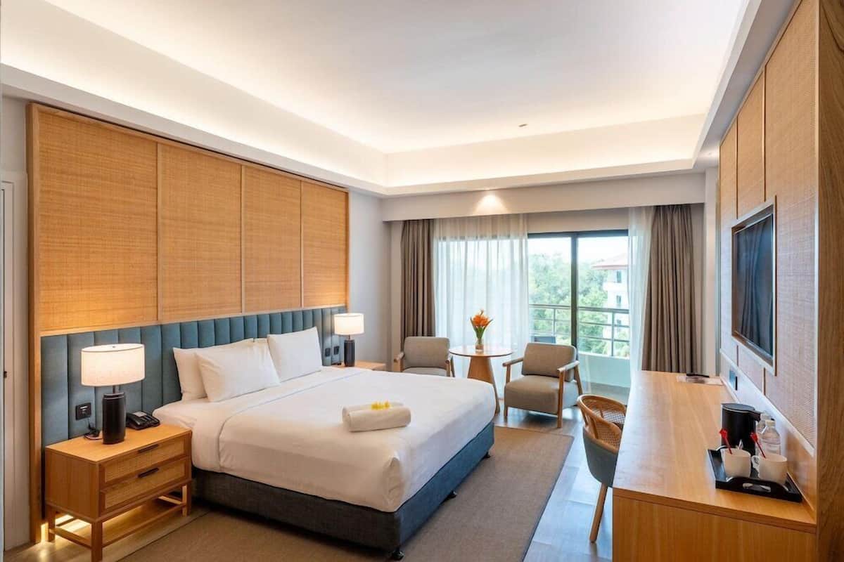Ein Hotelzimmer mit Bett, Nachttischen, einem Schreibtisch, Stühlen, einem Fernseher und einem Fenster mit Vorhängen.