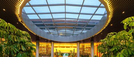 A modern hotel lobby with a large skylight, columns, and indoor plants.