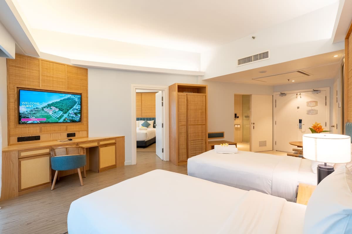 Ein Hotelzimmer mit Fernseher, zwei Betten, einem Schreibtisch und einem Sessel.