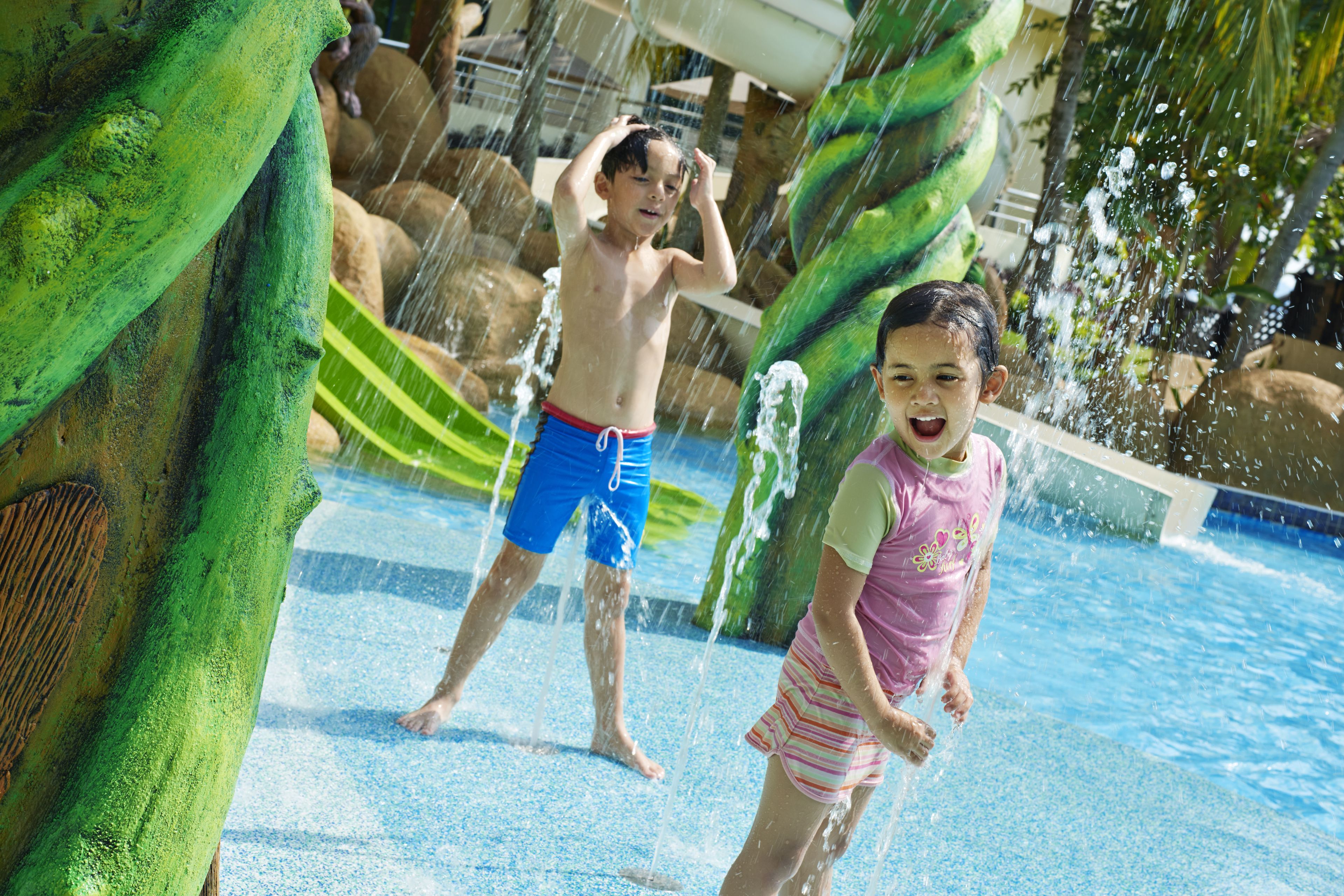 Two children playing in a water park with slides and water features.