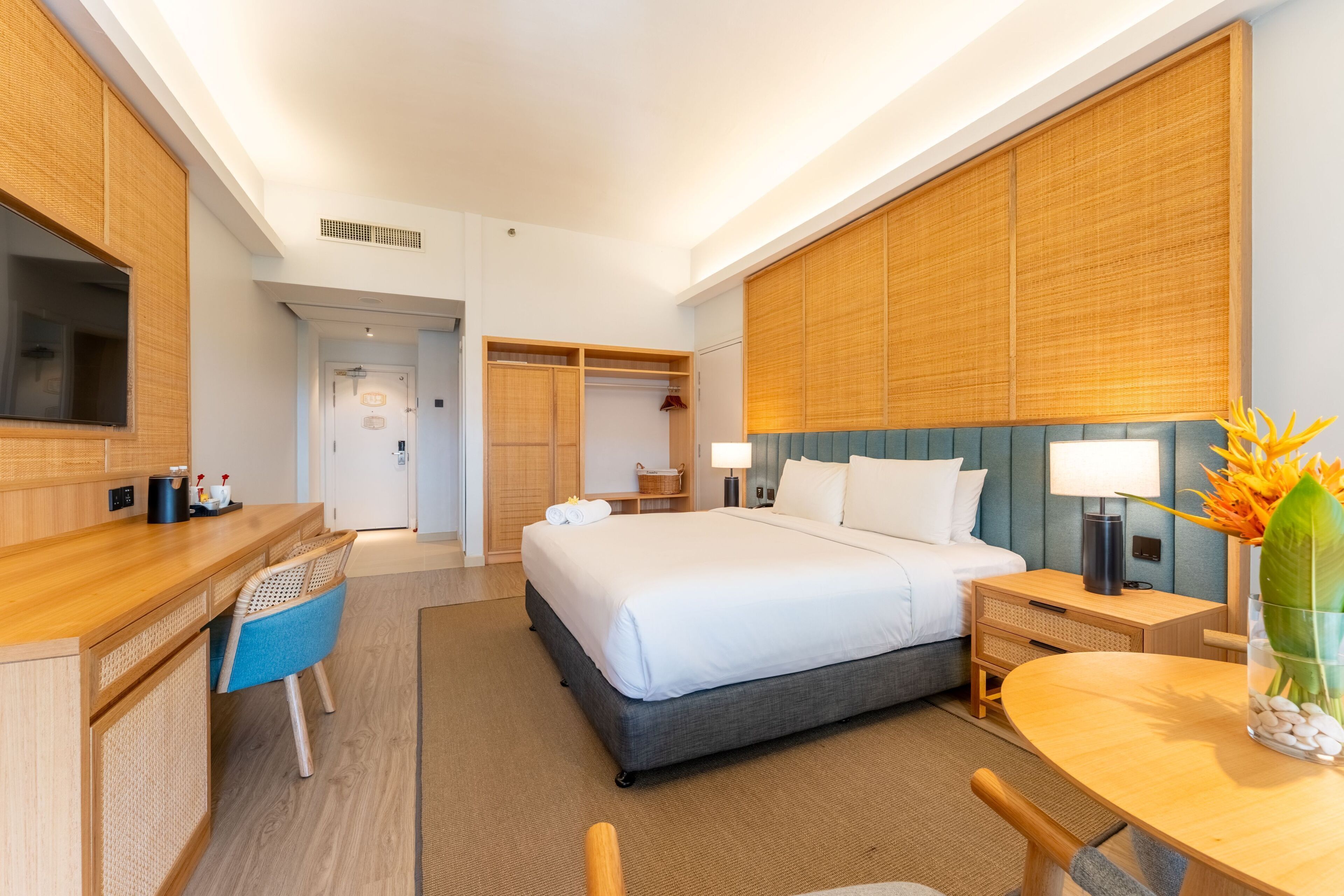 A hotel room with a bed, desk, chair, bedside table, lamp, and a vase with flowers.
