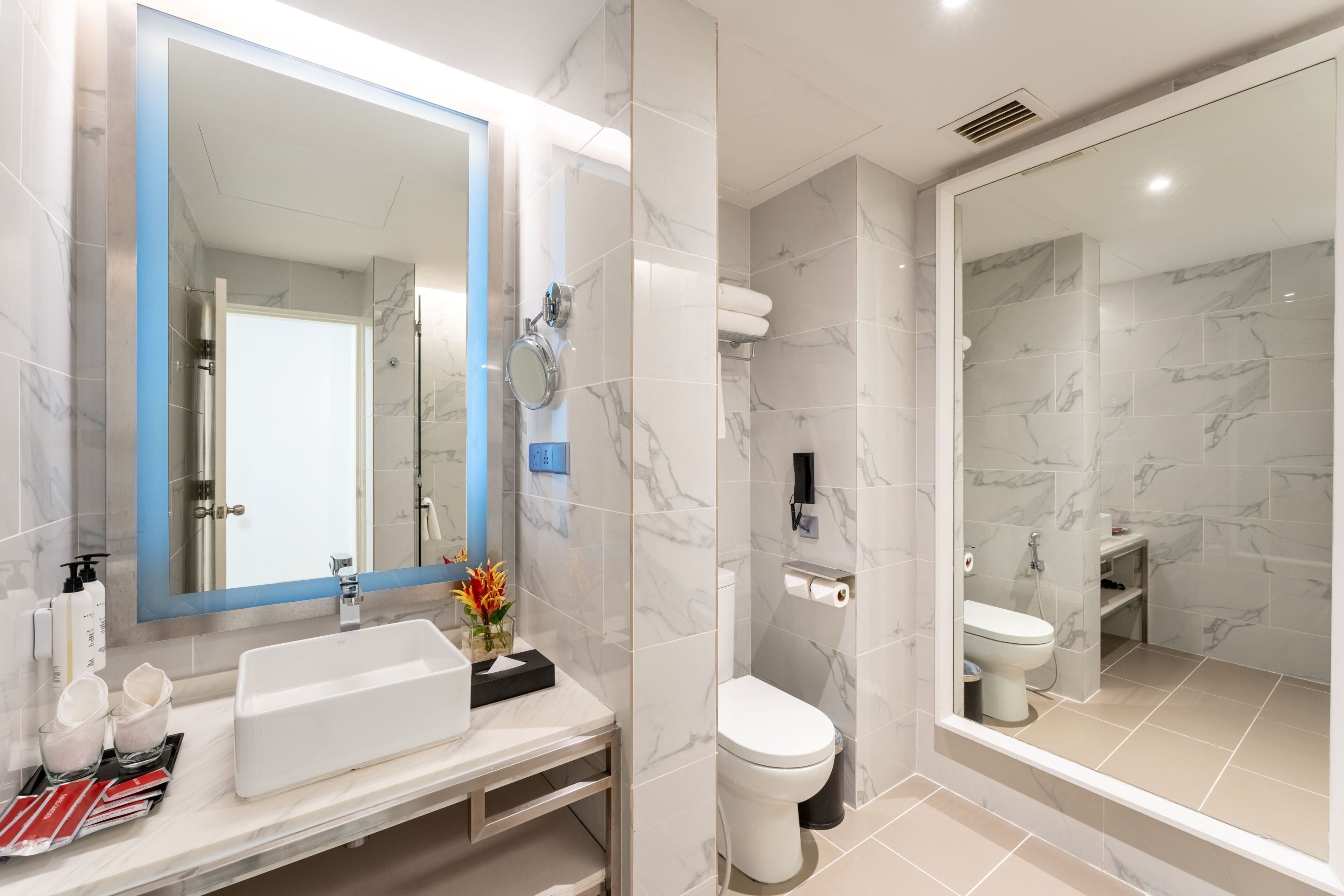 Un baño moderno con un espejo grande, un lavamanos, un inodoro y una zona de ducha.