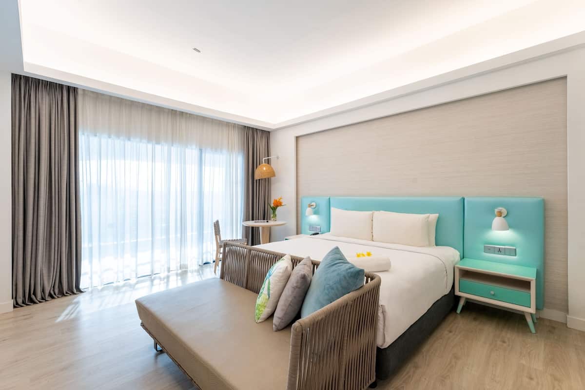 Ein modernes Hotelzimmer mit einem großen Bett, einem Nachttisch, einem kleinen Tisch und Blick ins Freie.