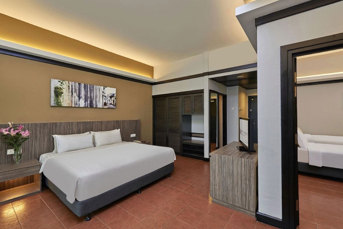 A hotel room with a large bed, a bedside table with a vase of flowers, a painting on the wall, and a separate seating area with a sofa.