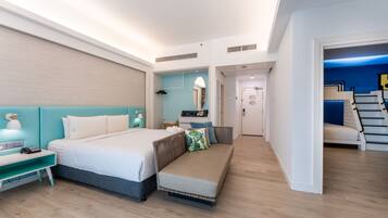 A modern hotel room with a bed, bedside table, and a bench. There is a mirror, a dresser, and a staircase leading to an upper level.
