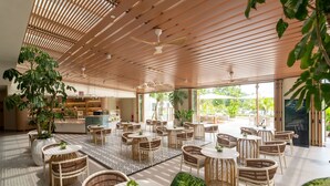 A spacious indoor area with multiple round tables and wicker chairs, surrounded by large potted plants and a patterned floor. - Swiss-Grand Beach Resort Kuantan (Kuantan)