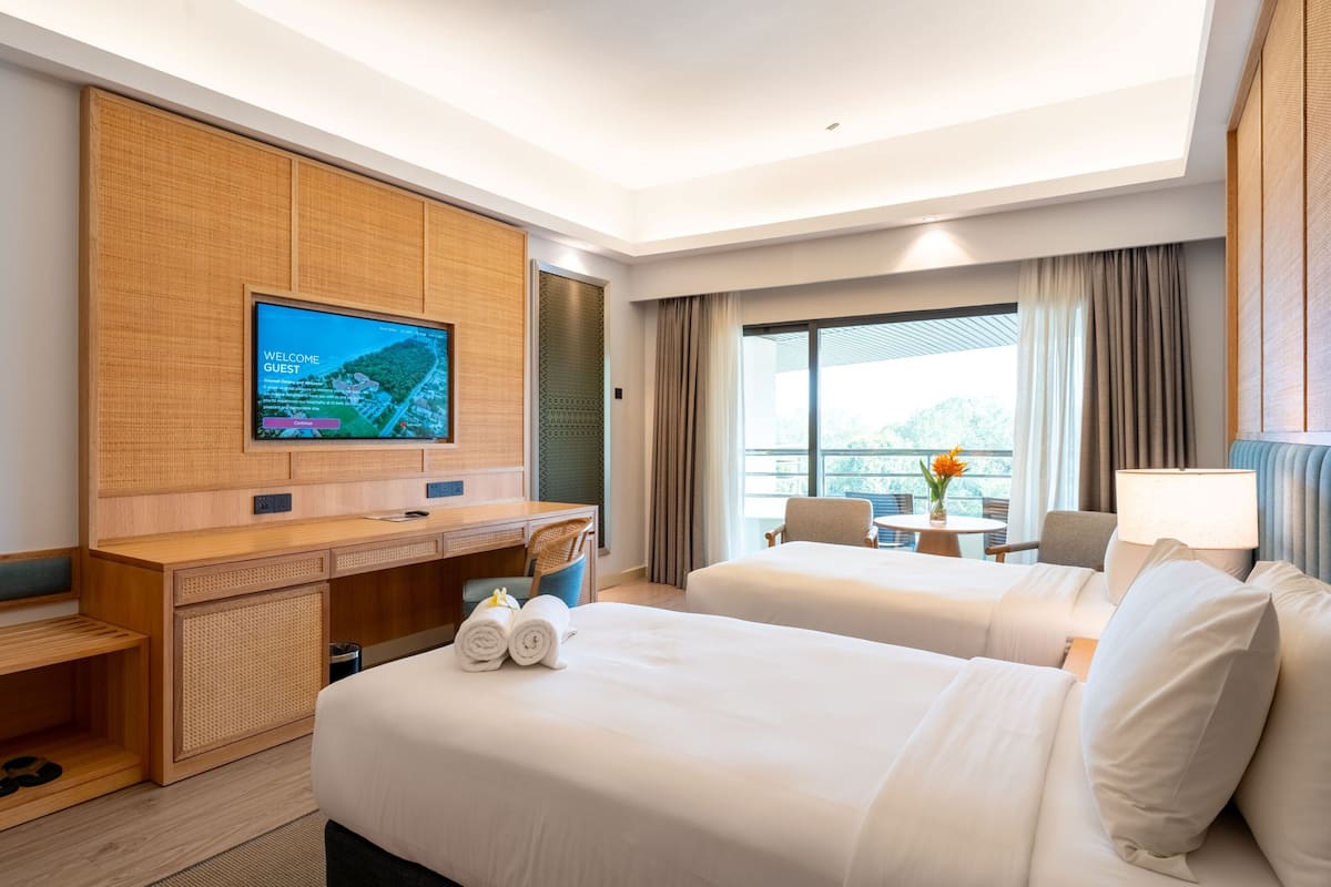 Ein Hotelzimmer mit Schreibtisch, zwei Betten, einem Fernseher und Blick ins Freie.