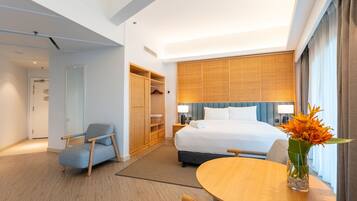 A hotel room with a bed, a wooden wardrobe, a seating area with a table, and a vase with flowers.