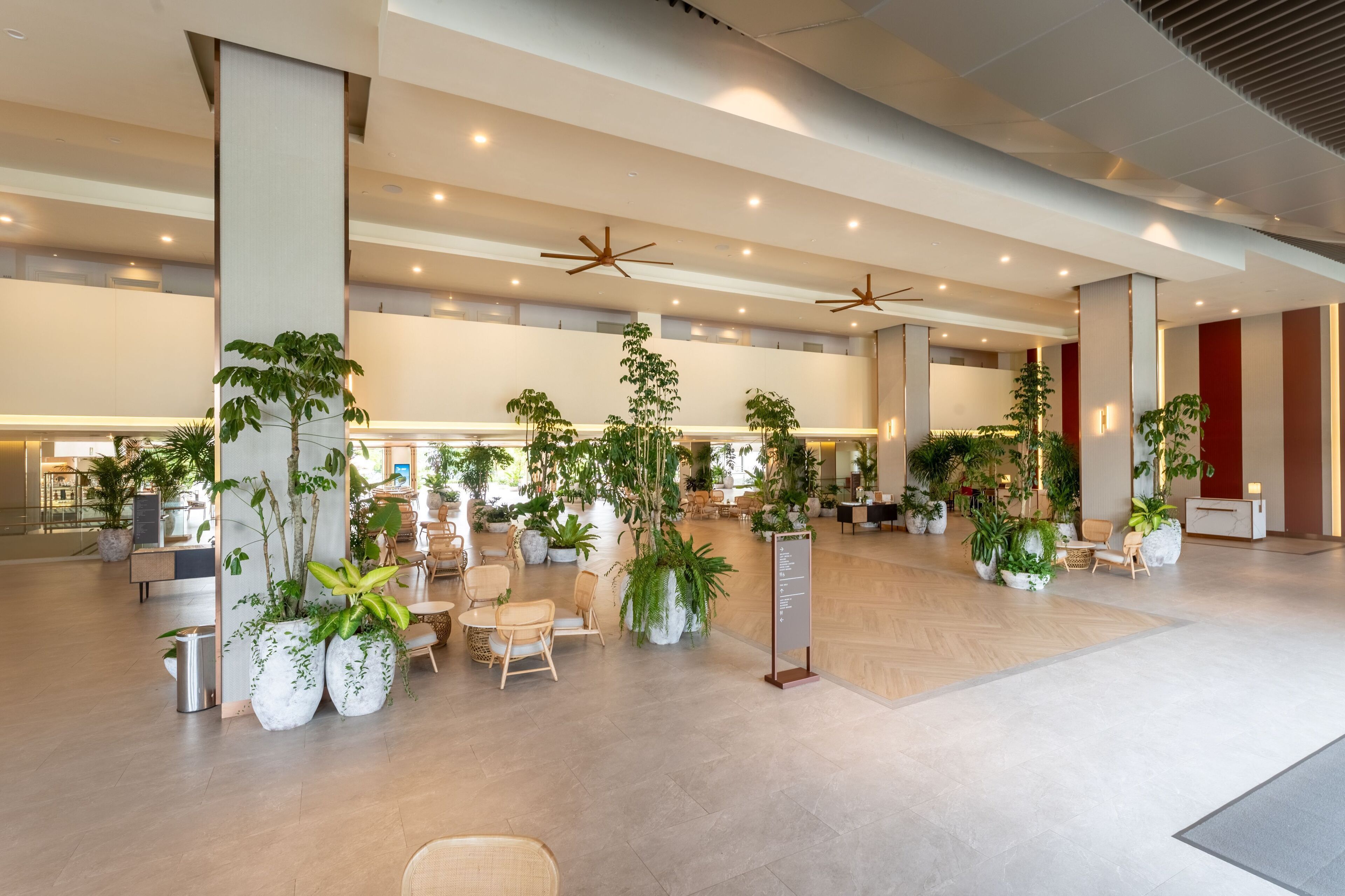 A spacious lobby with multiple seating areas, large potted plants, and ceiling fans.