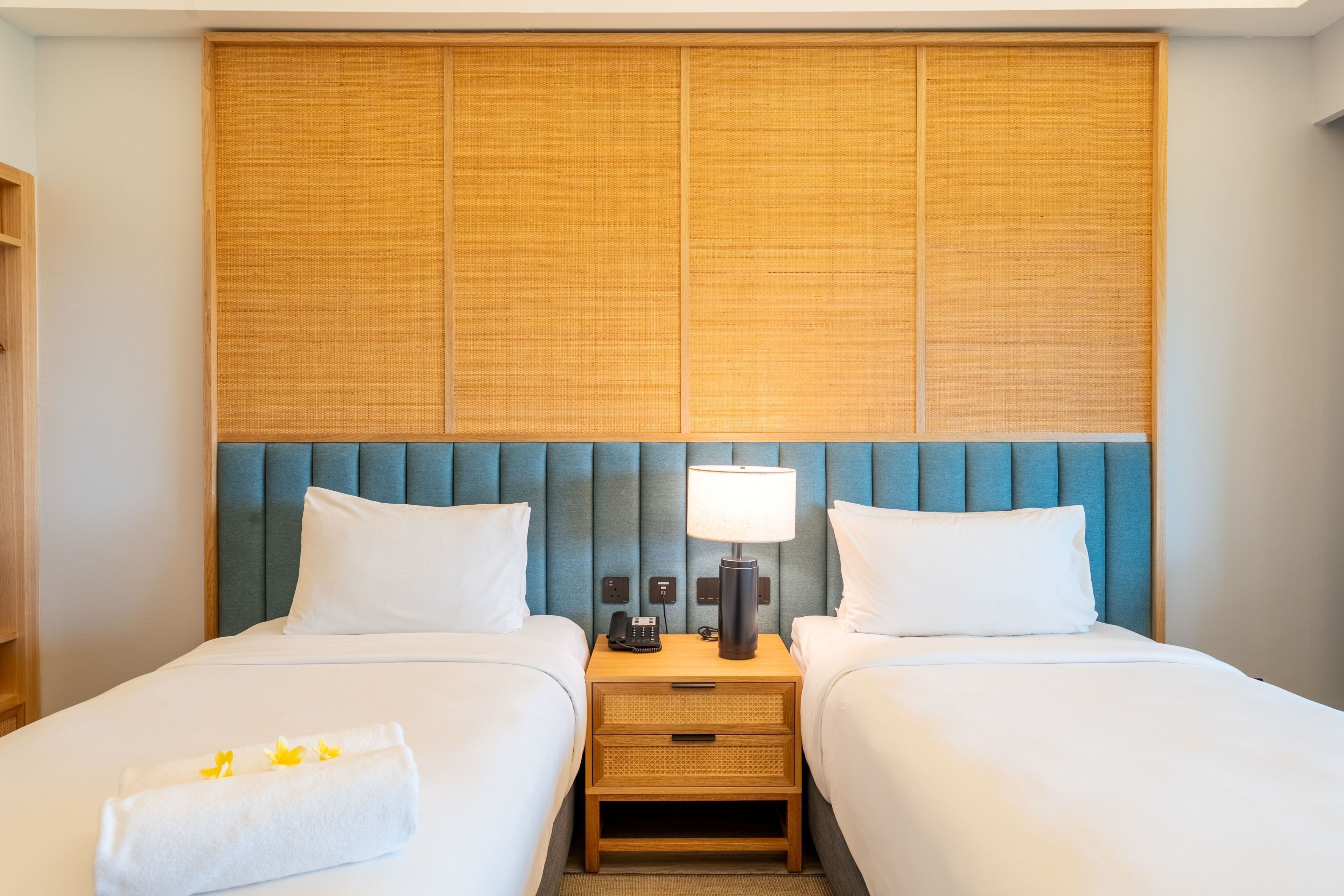 A hotel room with two beds, a headboard with vertical panels, bedside tables with lamps, and a telephone.