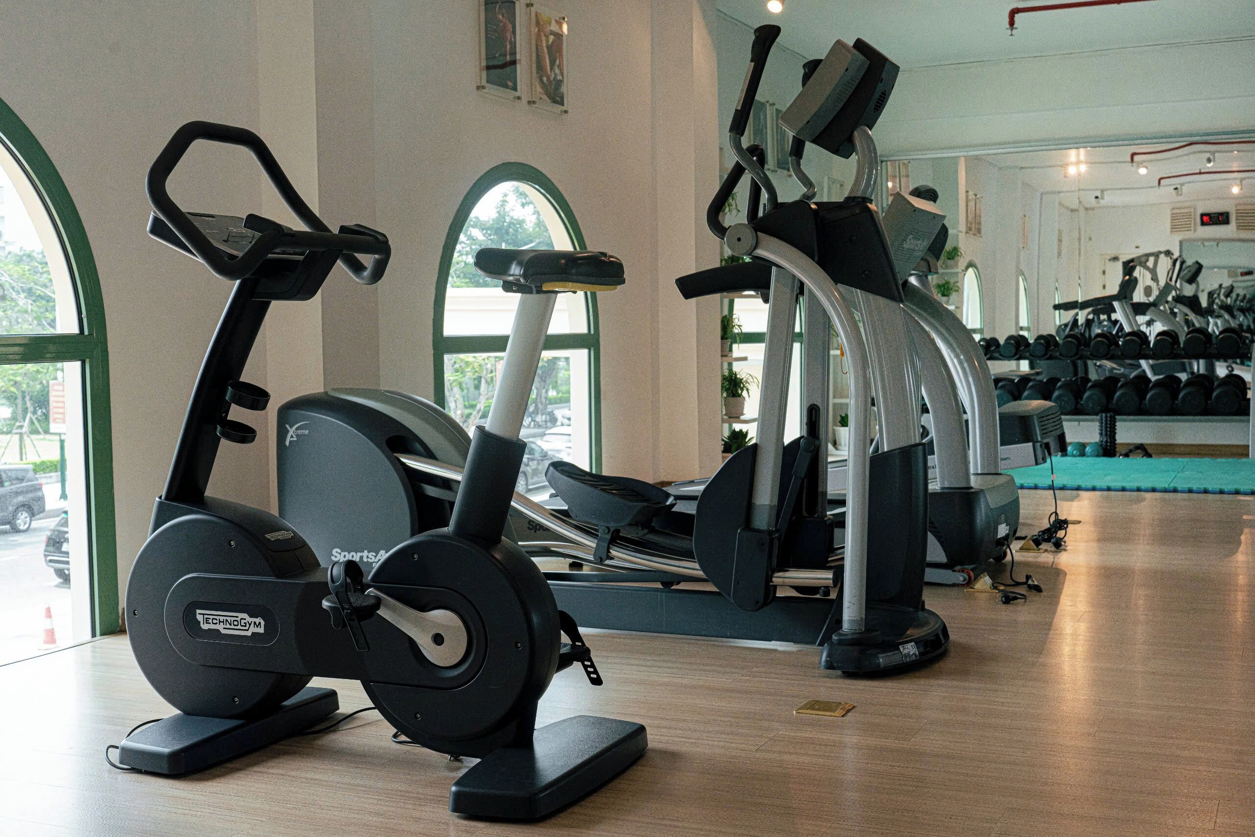 Un gimnasio con máquinas de cardio, equipo de pesas y un espejo grande.