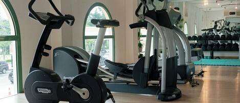 Un gimnasio con máquinas de cardio, equipo de pesas y un espejo grande.